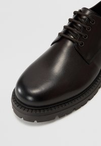 Zwarte leren schoen met ronde neus, vetersluiting en stevige rubberen zool met zichtbare profilering en stikseldetails.