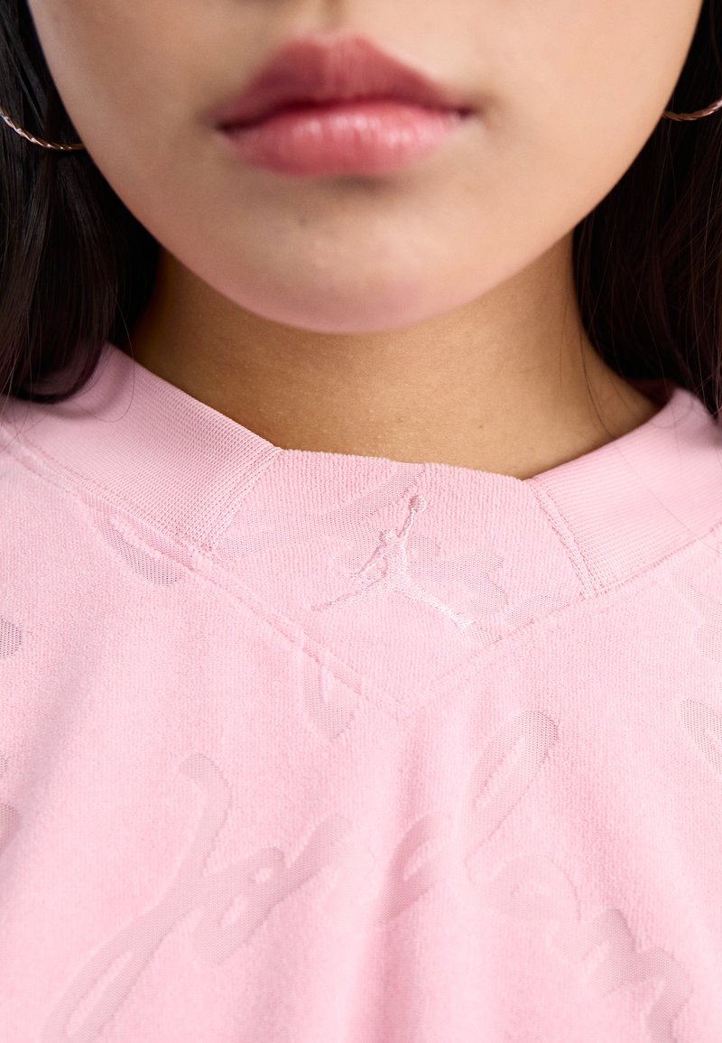 Felpa rosa con logo 'Jordan' in rilievo e silhouette di un giocatore. Il materiale sembra morbido con una finitura testurizzata e colletto.