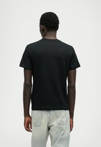 Svart bomull T-skjorte med rund hals, korte ermer og enkel bakdesign. Kombinert med lysegrå denimjeans.