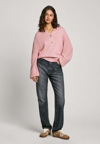 Suéter de punto rosa con mangas anchas, presenta botones de madera. Combinado con jeans de denim oscurecidos y zapatillas con estampado de leopardo.