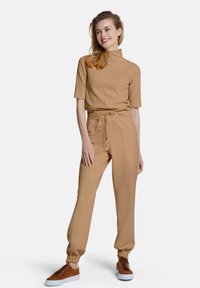 Tan geribbeld top met korte mouwen, gecombineerd met bijpassende joggers met treksnaren en elastische manchetten, gestyled met bruine sneakers en een strakke silhouet.