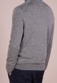 Grå stickad tröja med rund halsringning, ribbade mudd och nederkant. Mjuk textur, med en sömlös design vid axlar och rygg.