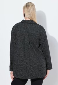 Zwarte button-up blouse met lange mouwen en een rugplooi; heeft een klassieke kraag en manchet met één knoop.