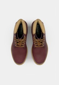 Zapatos de cuero marrón con cuello acolchado beige, cordones redondos y suela de goma. Presenta el logotipo en la lengüeta y un forro interior texturizado.