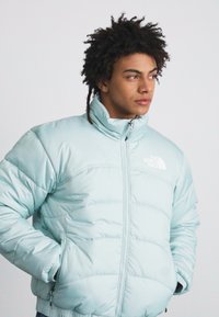 Giubbotto imbottito azzurro chiaro con colletto alto, chiusura con zip e logo bianco sul lato sinistro del petto. Presenta un design trapuntato e imbottito per l'isolamento.