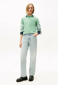 Sudadera verde con la impresión "TOMMY JEANS" y mangas a rayas, combinada con jeans de pierna recta en azul claro y zapatos gruesos negros.