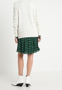 Biały sweter z dzianiny o teksturowanej fakturze, z długimi rękawami, na zielonej plisowanej sukience z białymi wzorami gwiazdek. Obuwie: białe botki za kostkę.