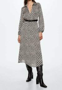 Vestido midi a rayas en blanco y negro con mangas largas, escote en V y cintura ajustada, combinado con botas negras de tacón alto.