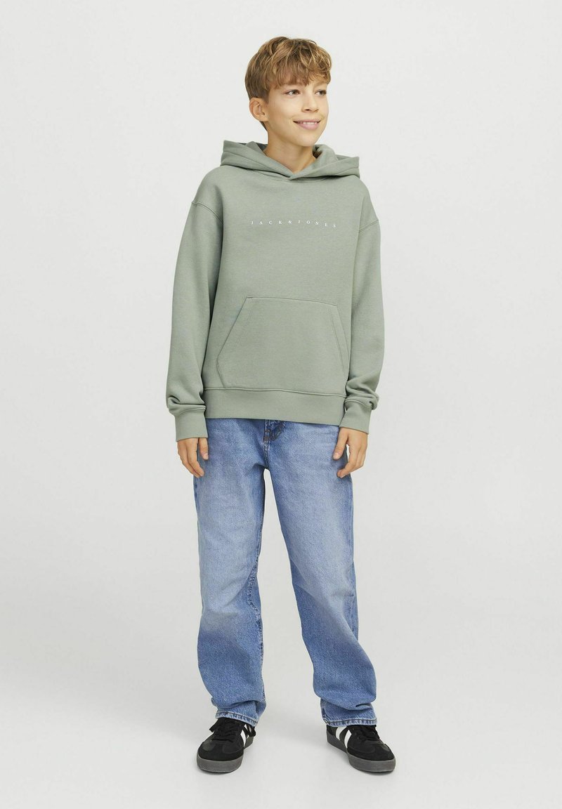Sudadera verde claro de mezcla de algodón, con un bolsillo frontal tipo bolsa y texto del logo en blanco. Combinada con jeans azul claro y zapatillas negras.