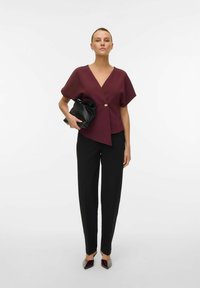 Top avvolgente bordeaux con maniche corte e un bottone dorato, abbinato a pantaloni dritti neri e una pochette nera. Ballerine grigie e bordeaux a punta.