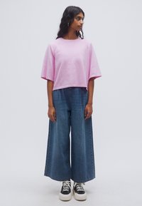 T-shirt courte rose clair à manches courtes, assortie à un jean en denim bleu à jambes larges et des baskets noires et blanches. Design simple et décontracté.