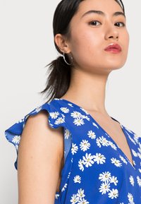 Vestido azul com padrão de margaridas brancas, mangas bufantes e decote em V profundo. Tecido suave com uma textura leve, ideal para o clima quente.