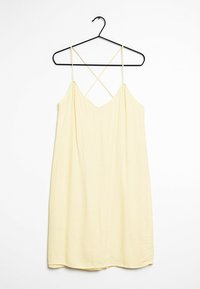 Gelbes Slipkleid mit dünnen gekreuzten Trägern, aus weichem Stoff gefertigt, mit einer leichten A-Linie und glatter Textur. Hängt an einem schwarzen Kleiderbügel.