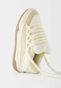 Sneaker v krémové barvě s měkkým, texturovaným fleece svrškem. Obsahuje silné tkaničky, gumovou podrážku a zaoblený design špičky.