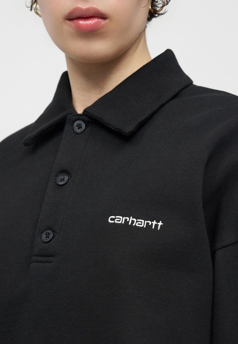 Gros plan d'une personne portant un polo noir boutonné avec un col et le logo brodé "carhartt" en blanc sur la poitrine.