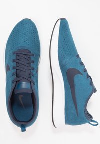 Běžecké boty Nike v tyrkysové semišové kůži s perforacemi, tmavě modrými tkaničkami, bílou podrážkou a tmavě modrým logem Swoosh. Pohled shora, viditelná vyjímatelná vložka.