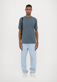 Grå kortærmet t-shirt, stof af medium vægt; parret med lyseblå løstsiddende jeans og hvide sneakers. Enkel design, ingen synlige mønstre.