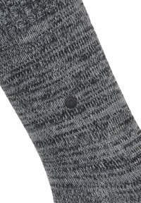 Calzino grigio lavorato a maglia con un motivo testurizzato, bordo a coste e un patch nero con logo vicino al fondo. Materiale morbido ed elastico.