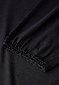 Svart långärmad tyg med elastiska manschettdetaljer. Texturen är slät och materialet verkar sträckt och kroppsnära.