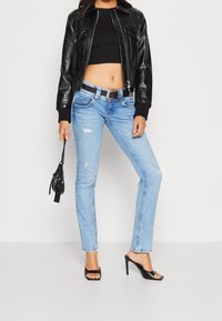 Jeans de mezclilla rectos de color azul claro con detalles desgastados, combinados con una chaqueta corta de cuero negra, una blusa negra y tacones de tiras.