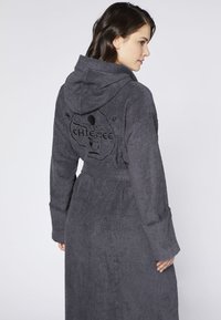 Grau gefütterter Bademantel aus Frottee, mit einem tonalen gestickten Design auf dem Rücken. Der Bademantel hat lange Ärmel und einen Gürtel in der Taille.