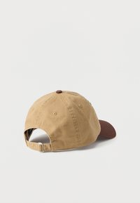 Kaki pet met een bruine klep, gemaakt van katoen. Heeft een afgeronde bovenzijde, een verstelbare band aan de achterkant en ventilatiegaatjes.