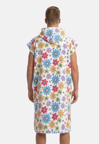 Hoodad strandponcho i mjukt frottématerial. Har färgglada blommönster i rött, blått, orange och lila mot en vit bakgrund.