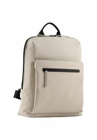 Mochila beige con una textura suave, que cuenta con un compartimento principal, un bolsillo frontal con cremallera y un asa negra. Detalle sutil del logo en la parte delantera.