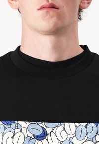 Sudadera negra con cuello redondo acanalado; presenta un diseño gráfico de formas abstractas en azul y blanco en la parte inferior. Textura suave.