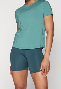 Vihreänsininen urheilupaita kosteutta siirtävästä materiaalista, jossa pyöreä kaula-aukko. Pari yhteensopivia vihreänsinisiä shortseja, sileä rakenne, istuva malli.