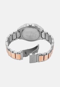 Hõbedane roostevabast terasest kell roosakullast aktsentidega käevõrul. Omab kuusnurksat kroonit ja poleeritud, tekstuuriga disaini.