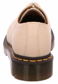 Beige Leder Schuhe mit abgerundetem Rücken, ausgestattet mit einer schwarzen Gummisohle mit strukturiertem Grip und gelben Nähten entlang der Kante.