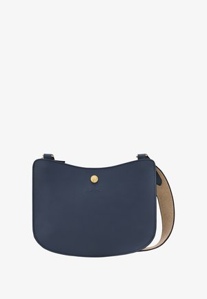 Navyblaue Leder-Umhängetasche mit gebogener Form, goldfarbener Knopfschließe, geprägtem Logo und breitem beigem Stoffriemen.