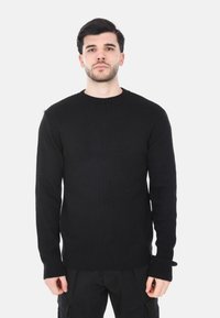 Maglione nero lavorato a maglia con scollo rotondo, texture a coste, maniche lunghe e una vestibilità comoda, abbinato a pantaloni cargo scuri.
