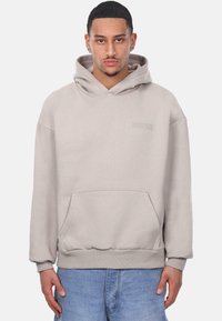 Svijetlosmeđi hoodie s prednjim džepom, rebrastim manžetama i rubom, sa suptilnim utisnutim logotipom. Napravljen od mekane, teksturirane tkanine.