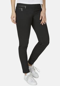 Svarta denimbyxor med smal passform, med två dragkedjefickor på framsidan. Bärs tillsammans med vita sportskor.