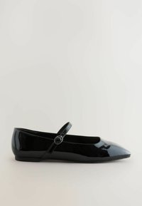 Zwart gepatenteerd leren platte schoen met een spitse neus, een ronde band met knoopdetail en een lage hak, met een gladde, glanzende textuur.