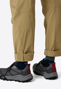 Beige cargo pants with rolled cuffs, paired with gray and red trail shoes. Shoes feature a textured sole and blue socks visible above the ankle.