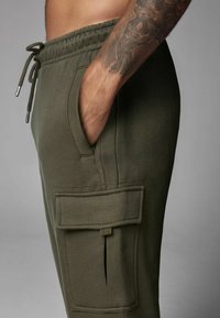 Olivgrüne Jogginghosen aus weichem Stoff, mit einer seitlichen Tasche mit Klappe, elastischem Bund und verstellbarem Kordelzug.