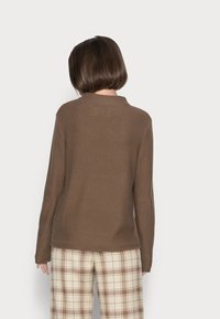 Pull en maille marron à manches longues et col rond, assorti à un pantalon à carreaux beige avec des accents marron.