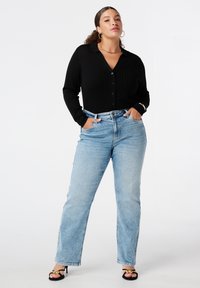 Zwarte geribbelde longsleeve overhemd met knopen gecombineerd met lichtblauwe recht gesneden jeans. Model draagt zwarte sandalen met bandjes. Eenvoudige accessoires.