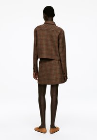 Brown checkered cropped jacket paired with a matching skirt, featuring long sleeves, a collar, and subtle stitching details. Suede slip-on shoes.