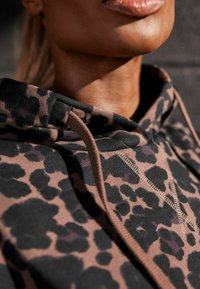 Sweat à capuche à imprimé léopard marron et noir avec un cordon de serrage. Tissu texturé et détails de couture contrastants.