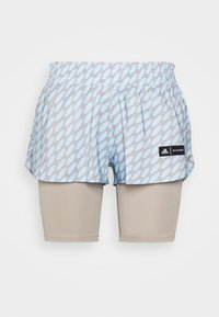 Svetle modré a šedé vzorované běžecké šortky navršené přes béžové těsné kompresní šortky s logy Adidas a Marimekko na pravé straně.