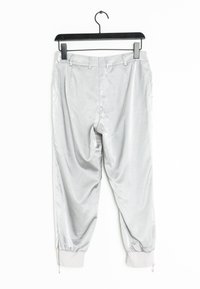 Ljust grå joggerbyxor som hänger upphängda. Funktioner inkluderar ett slätt, glänsande tyg, elastisk midja och dragkedja vid anklarna.