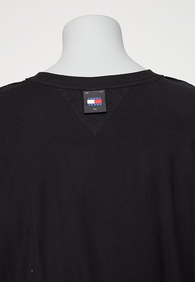 Camiseta de algodón negra con un profundo escote en V, etiqueta con la marca "TOMMY JEANS" y un corte relajado. Diseño minimalista sin patrones visibles.