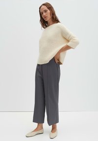 Cremefarbener, gestrickter Pullover mit weitem Ausschnitt und Dreiviertelärmeln, kombiniert mit hoch taillierter grauer Hose und beigen flachen Schuhen.