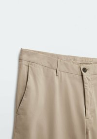 Pantaloni in cotone beige con chiusura a zip e bottone, tasche anteriori e una texture liscia. Presentano un davanti liscio e una vita standard.