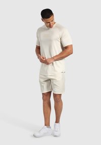 Ljusbeige atletisk tröja med texturerad tyg, kombinerad med ljusbeiga shorts som har sidopartier, bärs med vita sneakers.