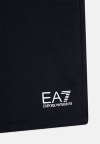 Tmavomodré športové šortky vyrobené z mäkkej tkaniny, s bielym logom EA7 Emporio Armani v dolnom ľavom rohu.